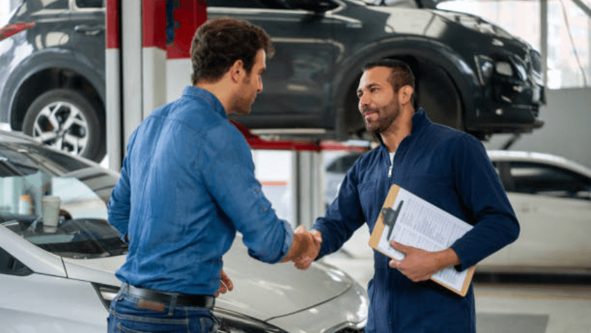 CARSTAR collision repair technician speaking with a customer about inspecting a damaged vehicle in a certified repair facility using advanced equipment to perform OEM-approved collision repairs and vehicle safety system calibration.